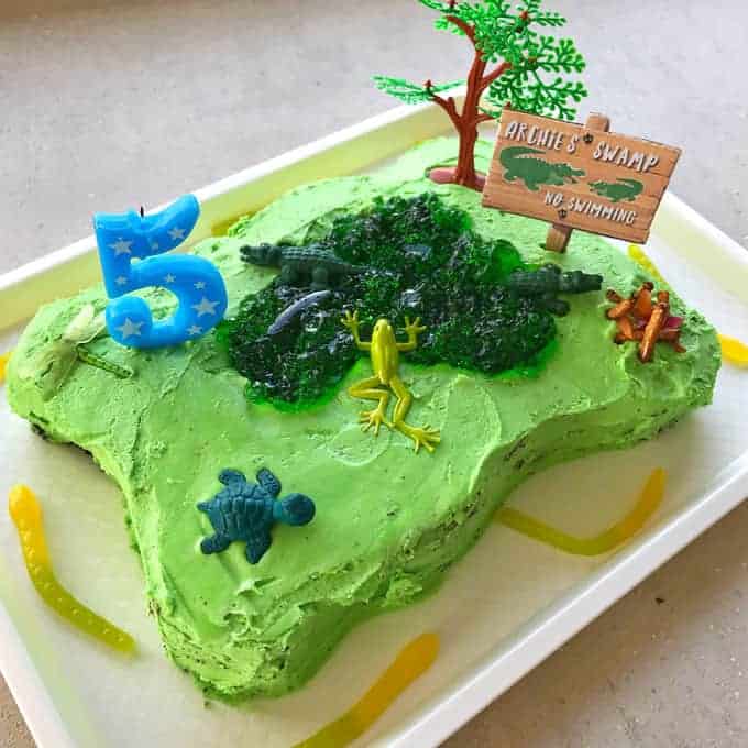 A birthday cake shaped like a green swamp sitting on a white tray. 