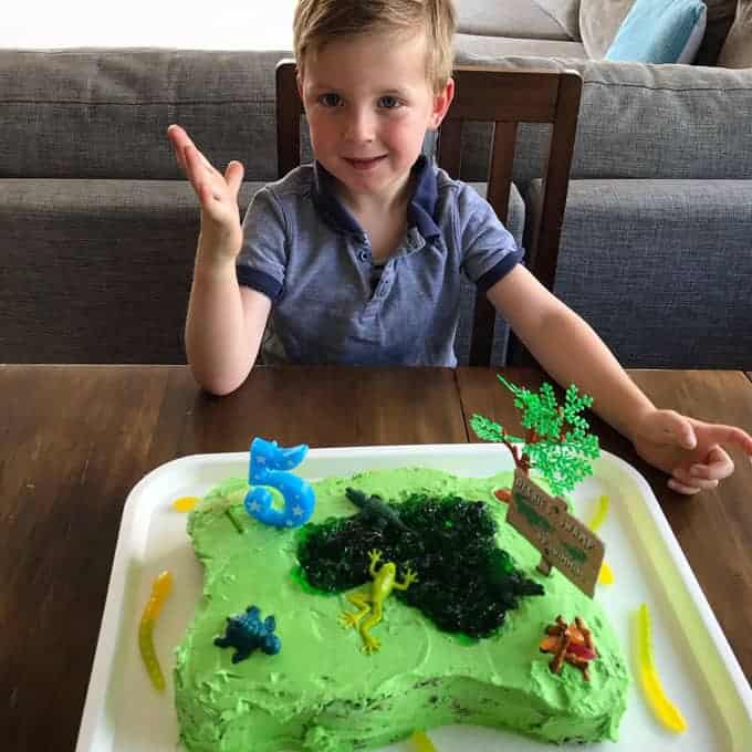 A boy sitting at a table with a green birthday cake decorated to look like a swamp.
