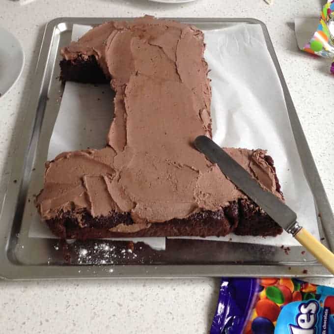 a chocolate number one cake being iced with chocolate icing.