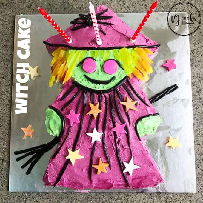 A birthday cake decorated to look like a pink witch sitting on a silver board.