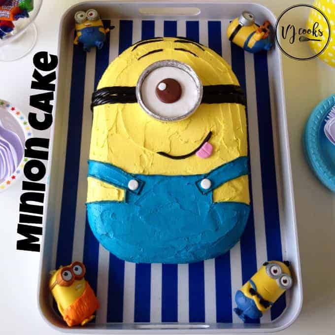 A birthday cake decorated to look like a minion sitting on a blue striped tray.