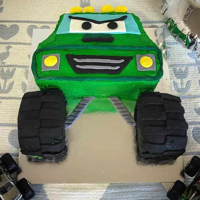 A cake decorated like a green monster truck sitting on a silver tray.