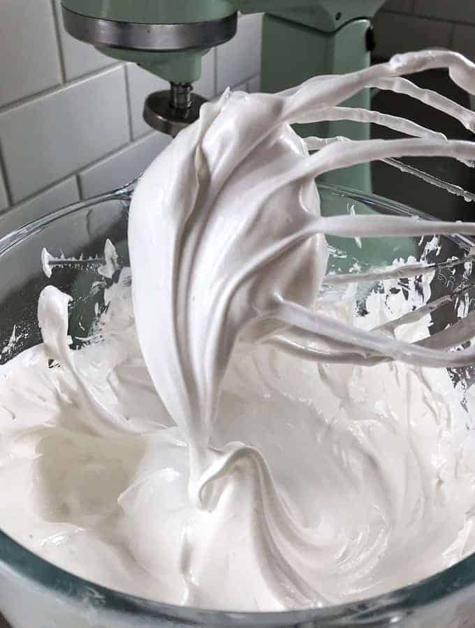 Mini Pavlovas with Raspberry Sauce A stand mixer beater covered in glossy, stiff peaks of white meringue sits above a glass mixing bowl filled with more meringue—perfect for creating delicate Mini Pavlovas.