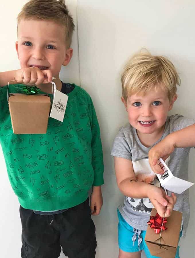 Two boys holding xmas gift boxes against a white wall.