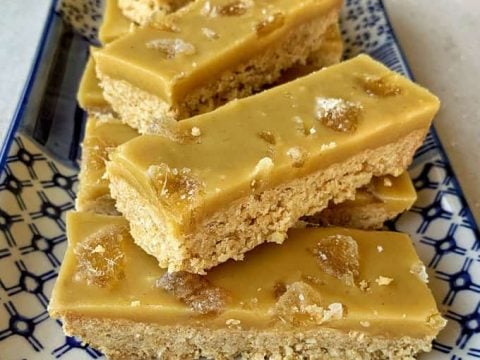 Rectangular slices of ginger crunch with a golden topping and crumbly base are arranged neatly on a patterned rectangular plate.
