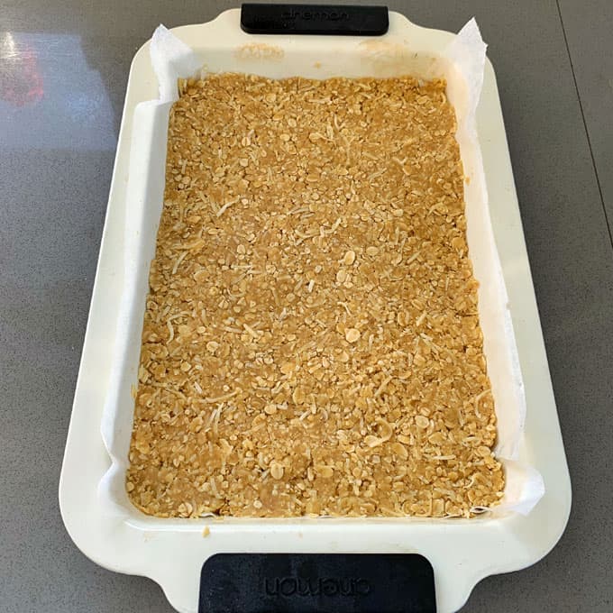 Ginger Crunch A rectangular baking dish lined with parchment paper contains an unbaked oat and coconut slice mixture, inspired by ginger crunch, evenly spread and ready to bake.