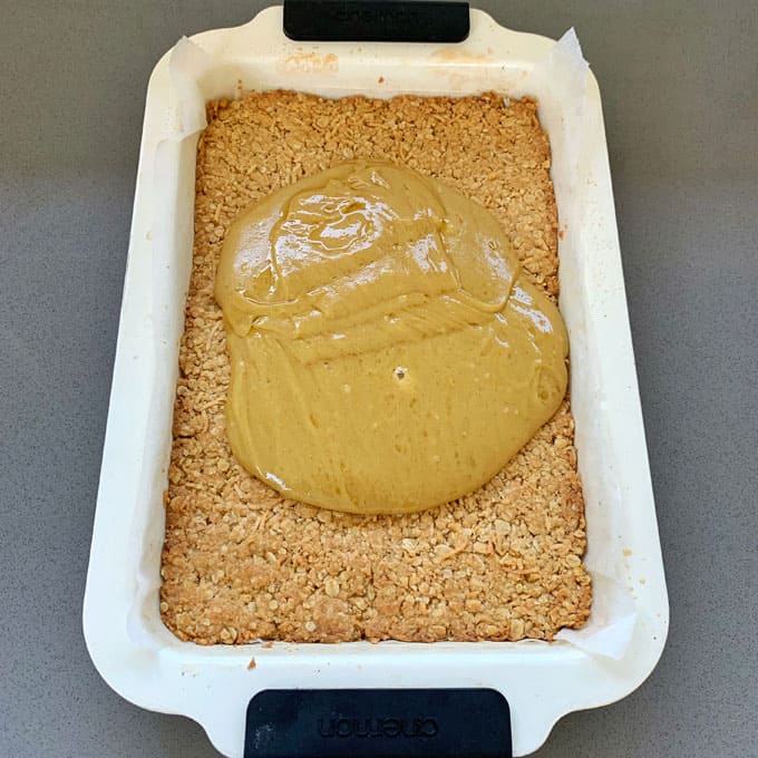 Ginger Crunch A rectangular baking dish with a layer of oat crumble and a large dollop of thick peanut butter mixture in the center, reminiscent of a classic ginger crunch treat.