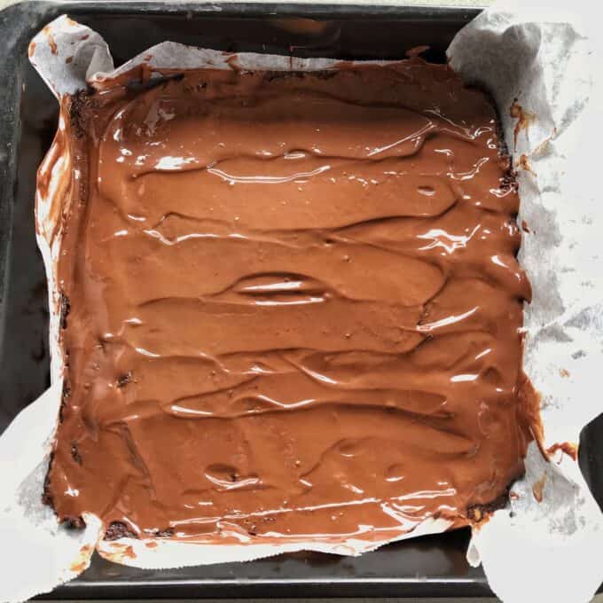 Raw Chocolate Slice A square baking pan lined with parchment paper holds a healthy raw chocolate slice, topped with a smooth layer of melted chocolate.