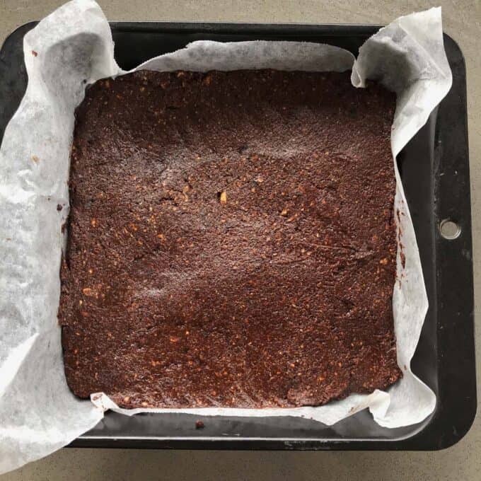 Raw Chocolate Slice A baking tray lined with parchment paper holds a large, uncut slab of healthy raw chocolate slice resting on a gray countertop.