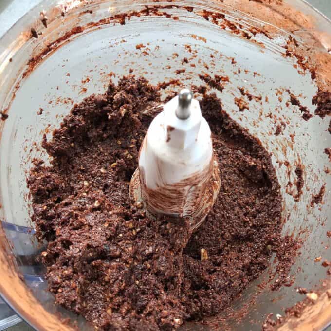 Raw Chocolate Slice Chocolate mixture with visible nut pieces in a food processor, showing blended ingredients attached to the central blade—perfect for making a healthy raw chocolate slice.