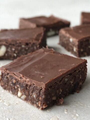 Several square pieces of healthy raw chocolate slice brownies with visible nut pieces are arranged on a light-colored surface.