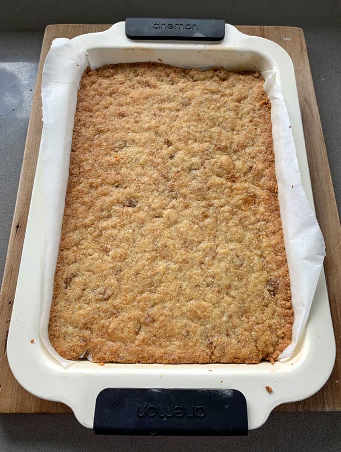 The cooked base of a weetbix slice sitting in a lined slice tray on a grey bench.