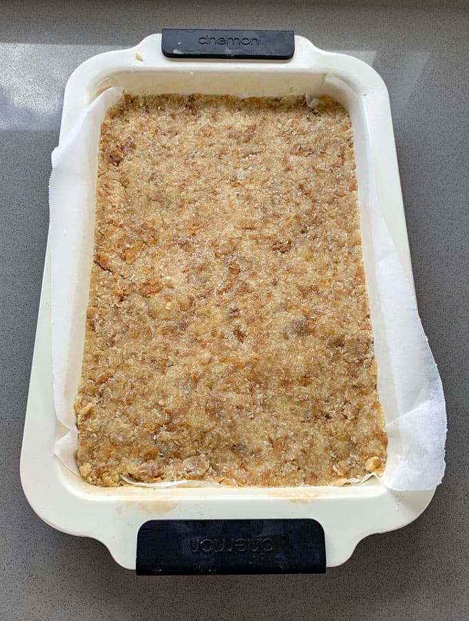 The base of a weetbix slice sitting in a lined slice tray on a grey bench.