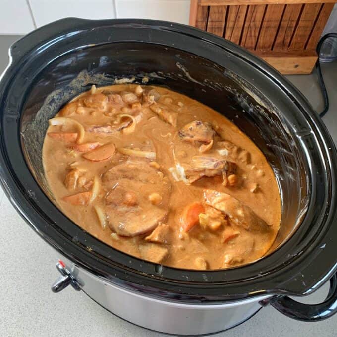 Slow Cooker Moroccan Lamb with Apricots A slow cooker Moroccan lamb stew filled with creamy sauce, tender meat, sliced onions, and vegetables sits on a kitchen counter.