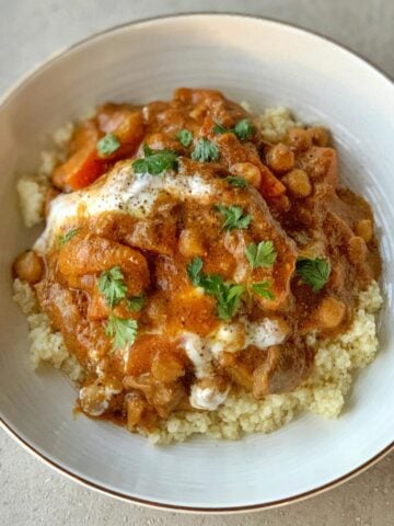 A bowl of couscous topped with a chunky slow cooker Moroccan lamb stew containing vegetables and chickpeas, garnished with fresh parsley.
