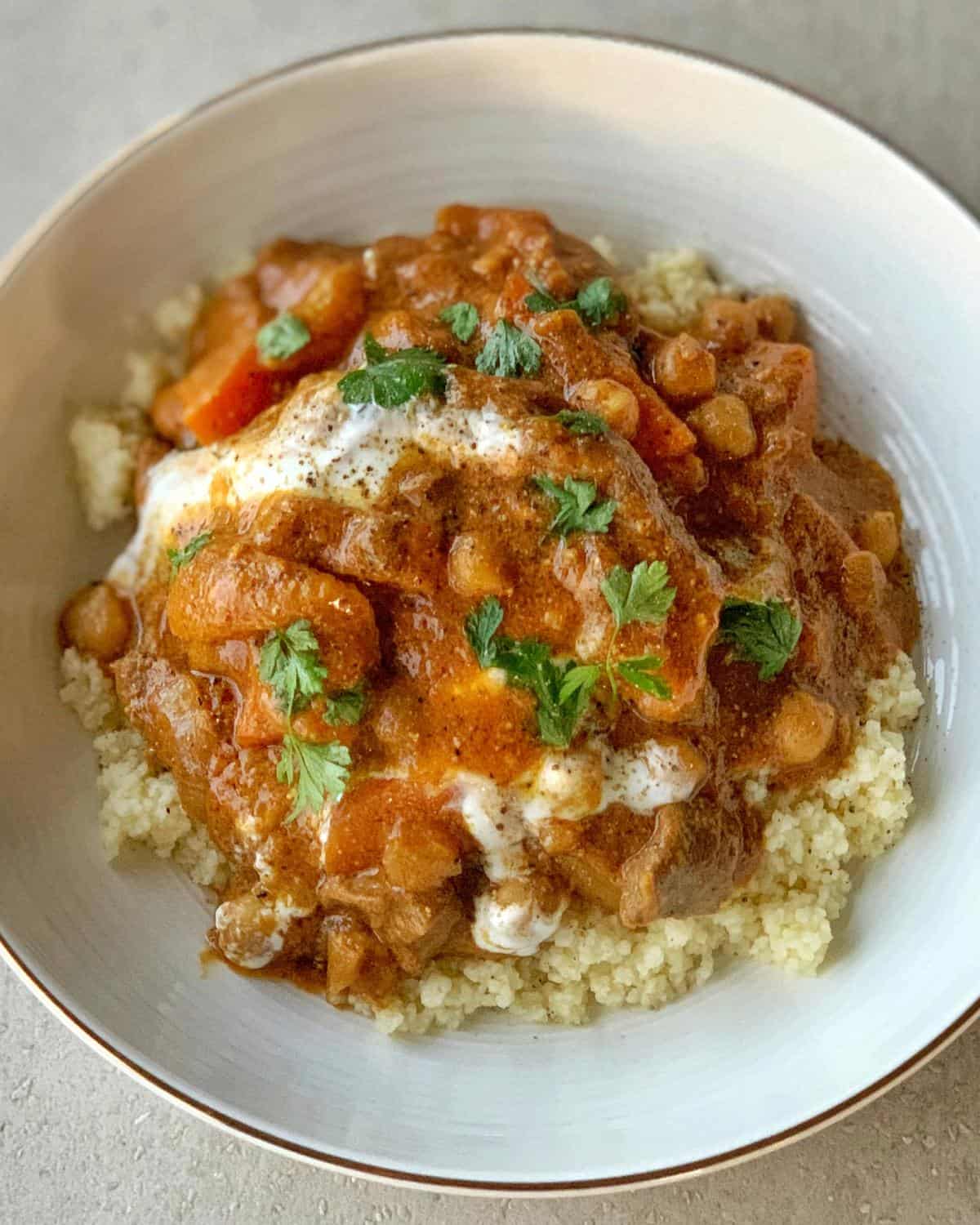 Slow Cooker Moroccan Lamb with Apricots A bowl of couscous topped with a chunky slow cooker Moroccan lamb stew containing vegetables and chickpeas, garnished with fresh parsley.