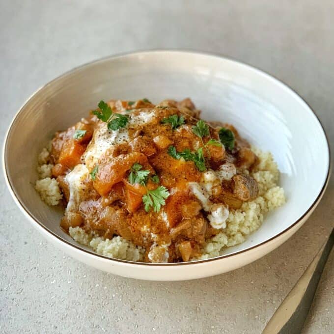 A bowl of couscous topped with a vegetable stew and tender slow cooker Moroccan lamb, garnished with fresh herbs and a drizzle of white sauce.