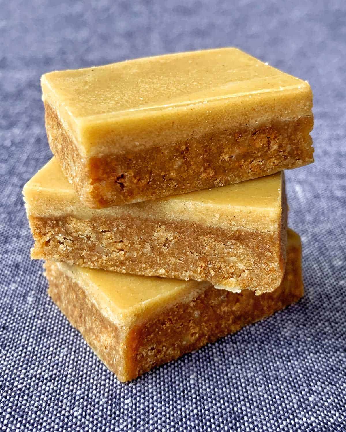 Three rectangular pieces of brown fudge are stacked on top of each other on a textured blue surface, reminiscent of a classic gingernut slice.