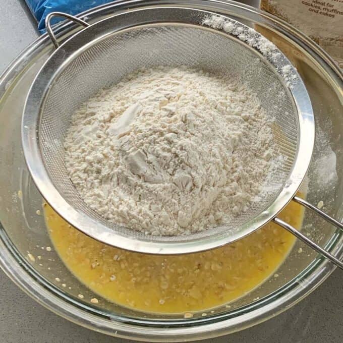 Easy Oaty Muffins A metal sifter holds flour over a glass bowl containing a wet mixture, ready to be combined for baking delicious oaty muffins.