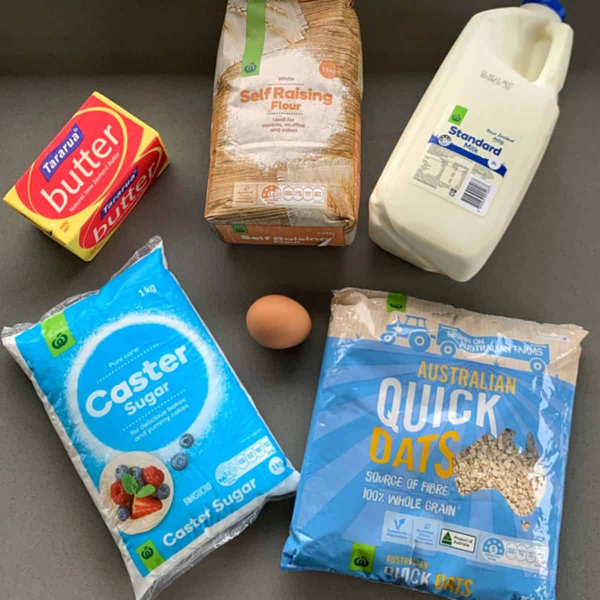 Easy Oaty Muffins Butter, self-raising flour, milk, caster sugar, an egg, and a bag of quick oats arranged on a countertop—everything you need to whip up tasty oaty muffins.