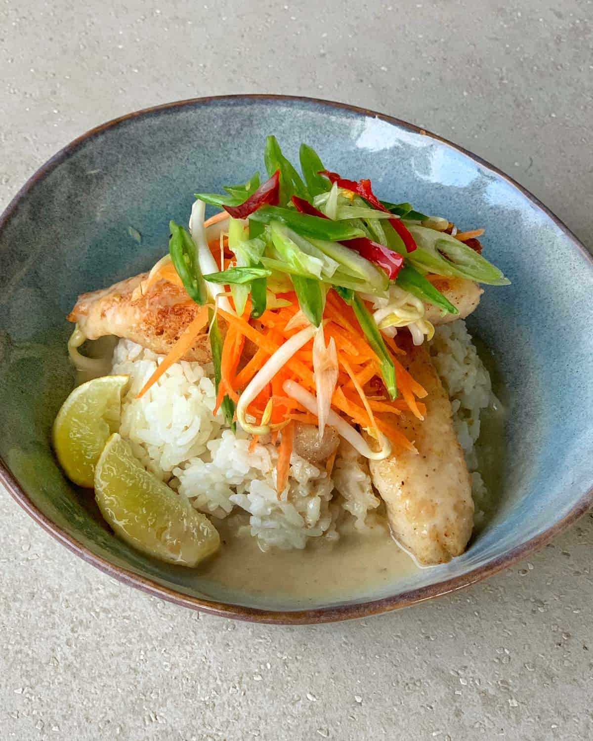 A bowl of white rice topped with chicken, shredded carrots, sliced green onions, bean sprouts, and served with lime wedges—perfect alongside pan fried fish with Thai green curry sauce.