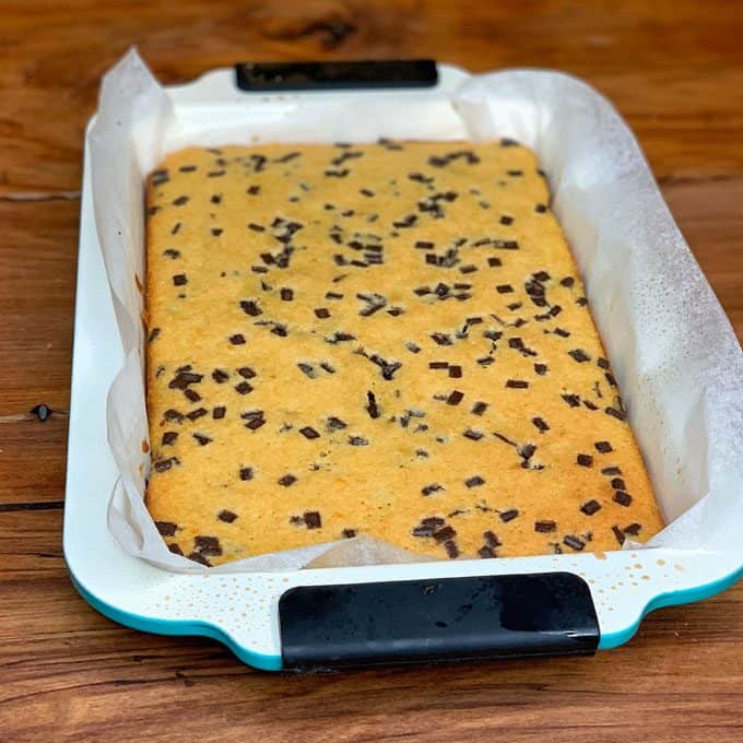 Orange Blondie with Dark Chocolate Chips An orange blondie with dark chocolate chips, baked in a parchment-lined pan, sits on a wooden surface.