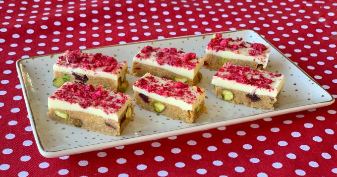 6 pieces of Cranberry and Pistachio slice sitting on a white platter on a red tablecloth.