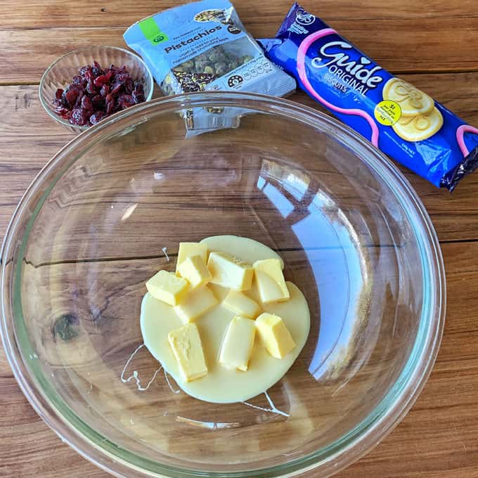 Butter and sweetened condensed milk in a glass bowl on a wooden bench.