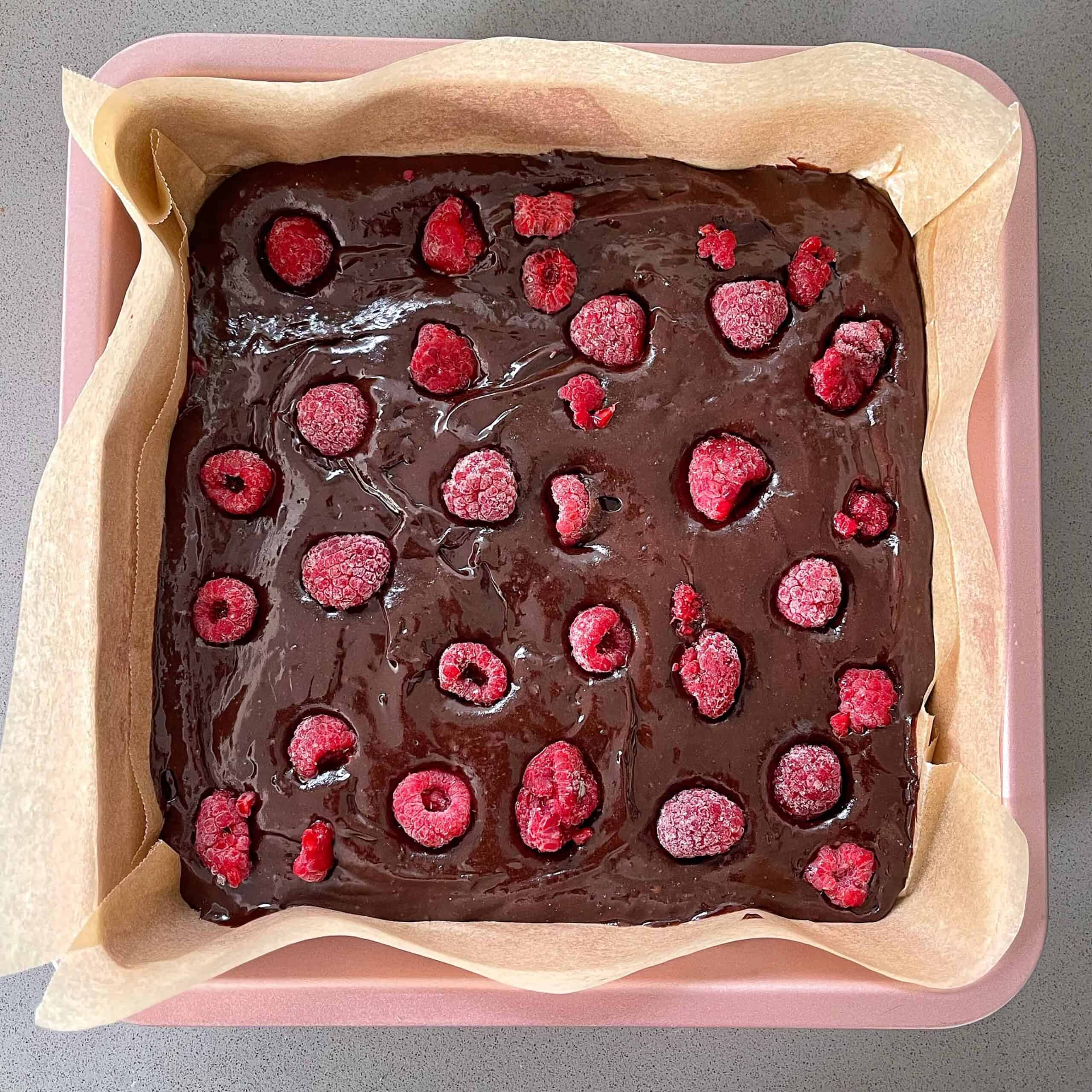 Uncooked chocolate raspberry brownie in a line baking tin.