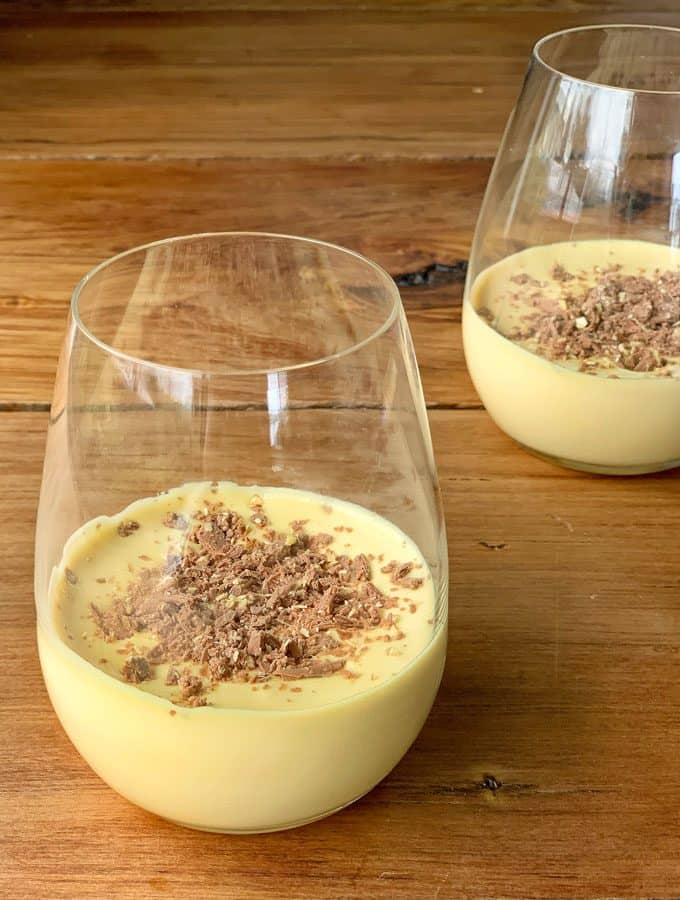 Caramilk Mousse Two stemless glasses filled with creamy Caramilk Mousse topped with chocolate shavings sit on a wooden surface.