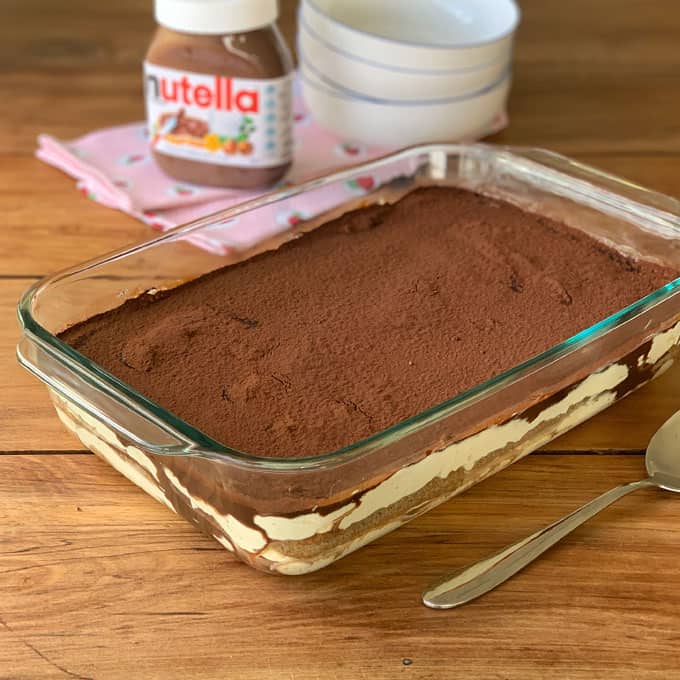 A large glass dish with Nutellamisu in it on a wooden bench.