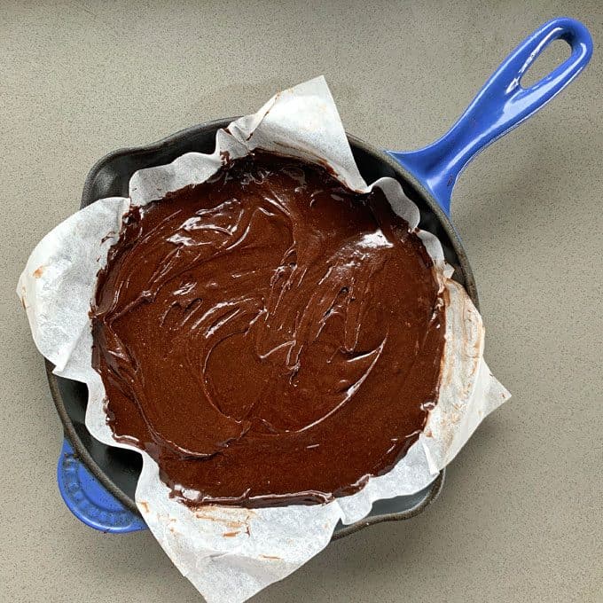 Chocolate and Raspberry Skillet Brownie A parchment-lined cast iron skillet filled with chocolate and raspberry skillet brownie batter, ready to be baked, sits on a gray countertop.