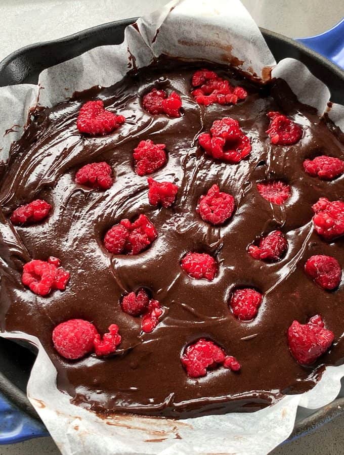 Chocolate and Raspberry Skillet Brownie A baking tray lined with parchment paper is filled with rich Chocolate and Raspberry Skillet Brownie batter, topped generously with fresh raspberries.