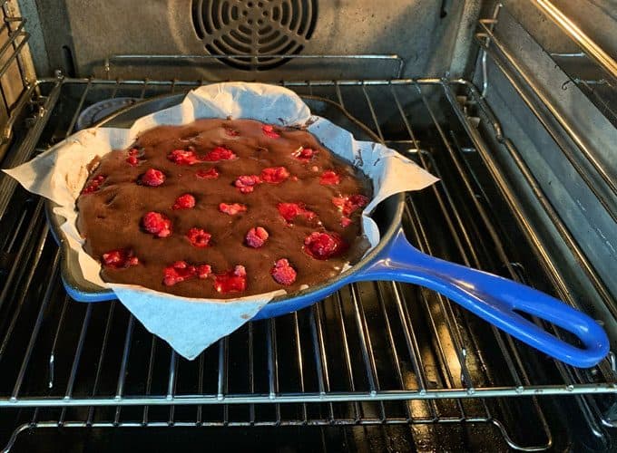 A cast iron skillet lined with parchment paper, filled with chocolate and raspberry skillet brownie batter, bakes in the oven.