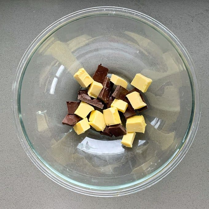 Chocolate and Raspberry Skillet Brownie A glass bowl containing chunks of dark chocolate and cubes of butter sits on a gray countertop, ready to be melted for a delicious Chocolate and Raspberry Skillet Brownie.