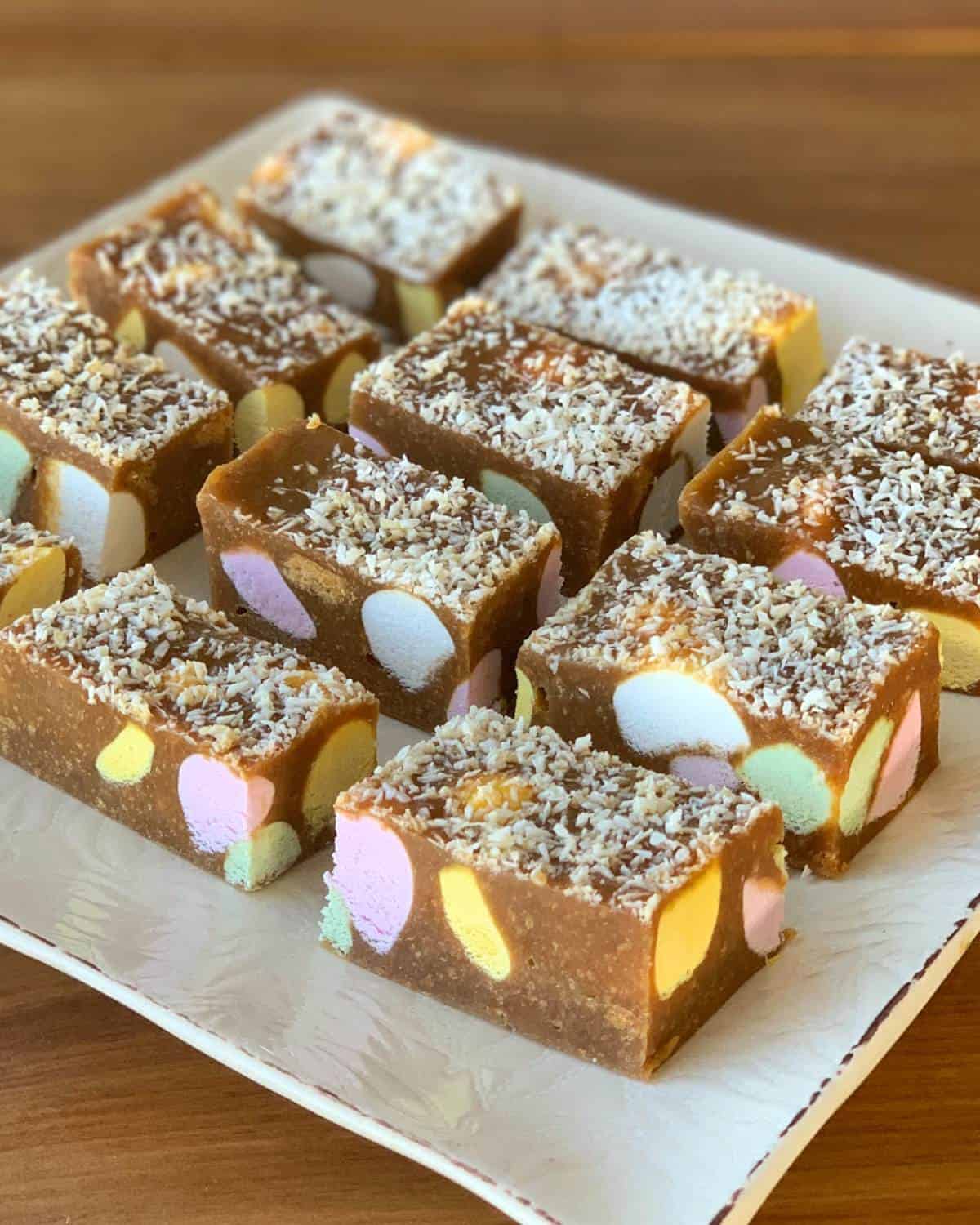 Rectangular pieces of Lolly Slice with colorful marshmallows and coconut flakes on top, arranged on a white plate.
