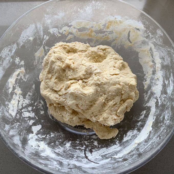 sausage and herb loaf A ball of raw dough, destined for a savory sausage and herb loaf, sits in a lightly floured clear glass mixing bowl on a countertop.