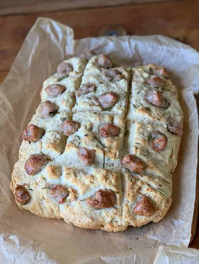A loaf of mushroom focaccia bread with browned dimpled spots and sprigs of rosemary, resting on parchment paper.
