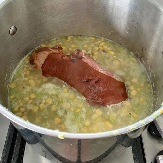 Corn and potato chowder with bacon hock A large pot on a stovetop contains split peas simmering in water with a pork hock, similar to the hearty base of corn and potato chowder bacon hock recipes.