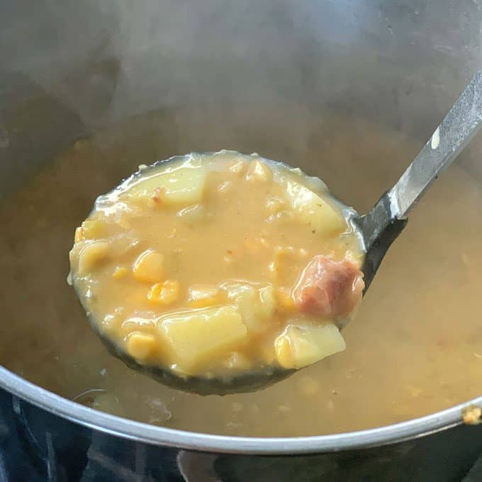 Corn and potato chowder with bacon hock A ladle of thick yellow split pea soup with chunks of potato, pieces of meat, and the smoky flavor of bacon hock held over a steaming pot.
