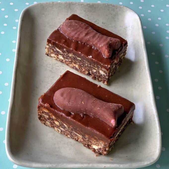 Chocolate Fish Slice Two rectangular chocolate fish slices, each topped with a chocolate fish-shaped candy, are placed on a beige plate against a blue and white polka dot background.