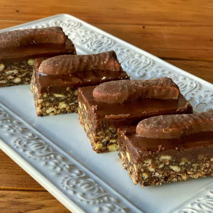 Chocolate Fish Slice Four chocolate fish slices topped with a layer of chocolate and a chocolate-coated biscuit, arranged on a decorative white rectangular plate.