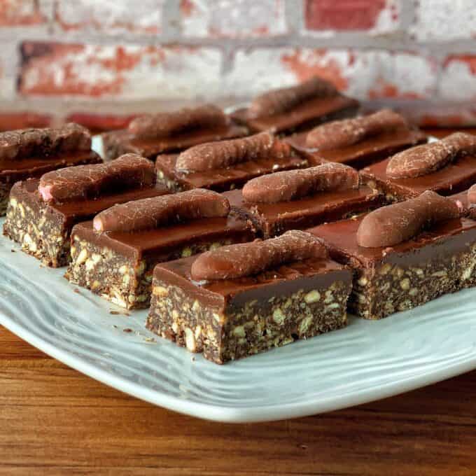Rectangular chocolate fish slices with a nutty base and a layer of chocolate on top, each topped with a chocolate-covered biscuit, arranged neatly on a white plate.