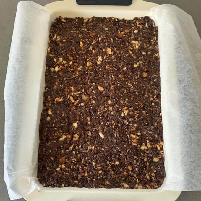 Chocolate Fish Slice A rectangular pan lined with parchment paper contains a pressed, crumbly chocolate and nut mixture—perfect for making a classic chocolate fish slice.