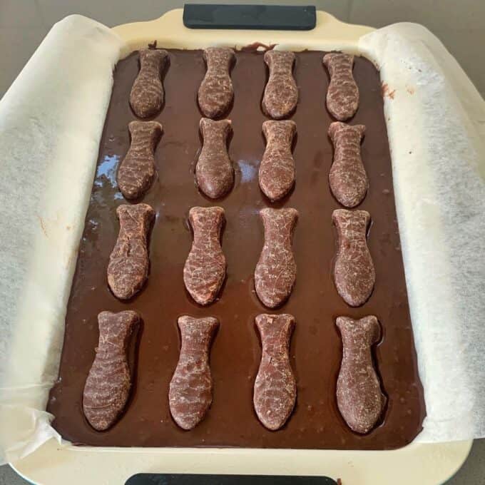 Chocolate Fish Slice A rectangular baking pan lined with parchment paper holds chocolate batter, topped with rows of fish-shaped cookies for a delicious chocolate fish slice.