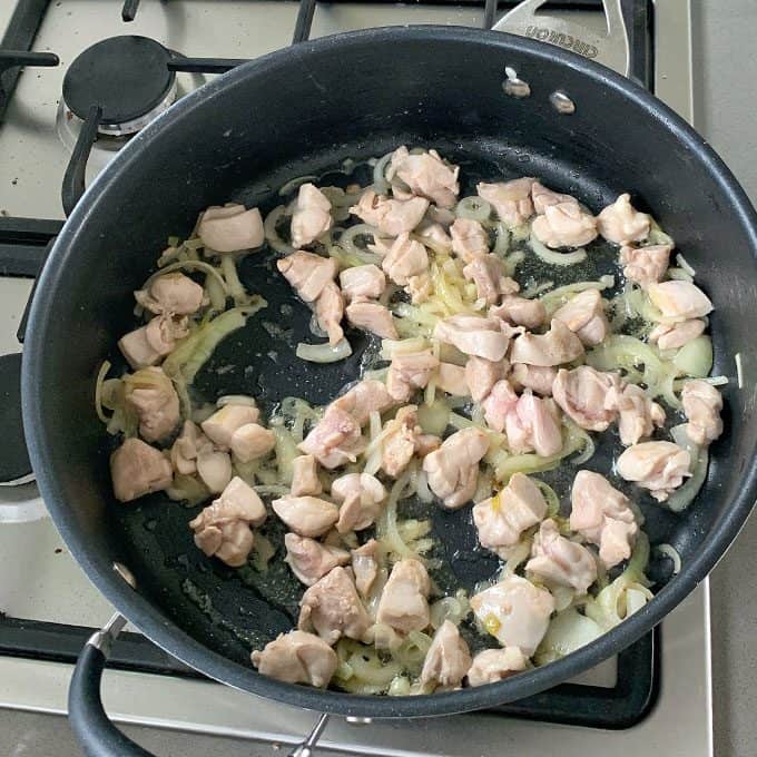 One pot chicken and pasta Chunks of raw chicken and sliced onions cooking in a black frying pan on a stove—the perfect start for a flavorful one pot chicken pasta.