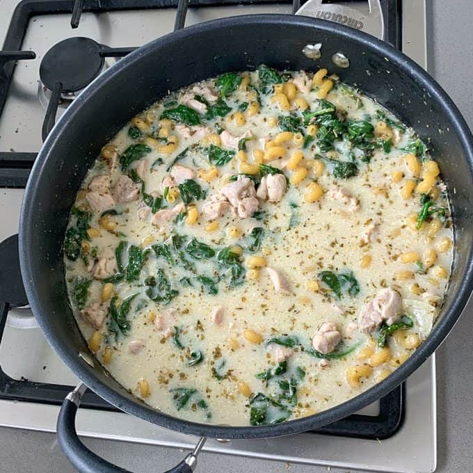 One pot chicken and pasta A black skillet on a stove contains a creamy one pot chicken pasta, blending tender chopped chicken, spinach, and pasta in a luscious white sauce.