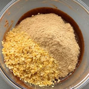 Easter Egg Slice Close-up of a bowl containing brown liquid, topped with piles of crushed cornflakes and a beige powder, resembling an Easter morning treat ready to be mixed.