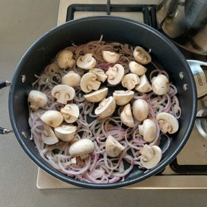 A pan on a stovetop contains sliced onions and halved mushrooms, the perfect base for a delicious Chicken Stroganoff.