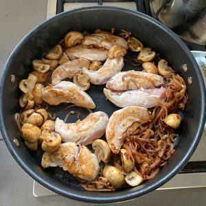 Chicken Stroganoff comes to life with chicken tenders, sliced mushrooms, and caramelized onions sizzling in a black skillet on the stovetop.